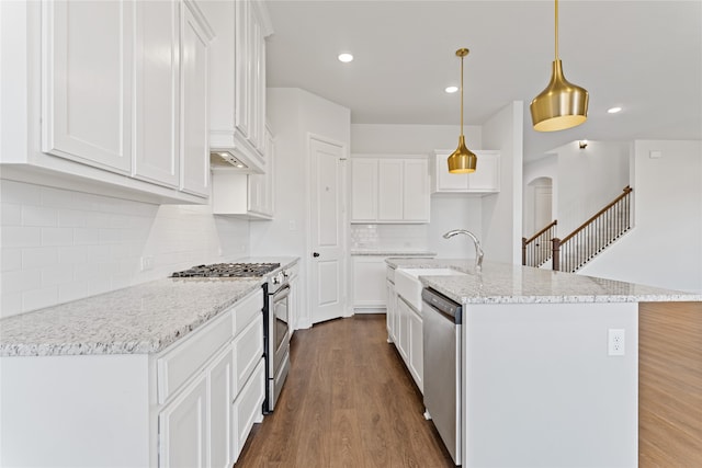 kitchen featuring dark hardwood / wood-style flooring, stainless steel appliances, decorative light fixtures, white cabinetry, and an island with sink