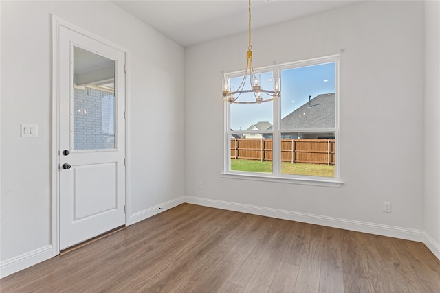 unfurnished dining area featuring wood-type flooring and an inviting chandelier