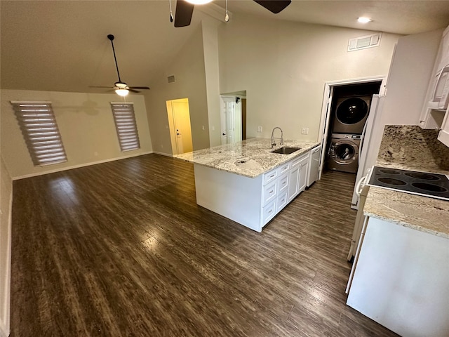 kitchen with stacked washing maching and dryer, dark wood-type flooring, light stone countertops, white cabinets, and high vaulted ceiling