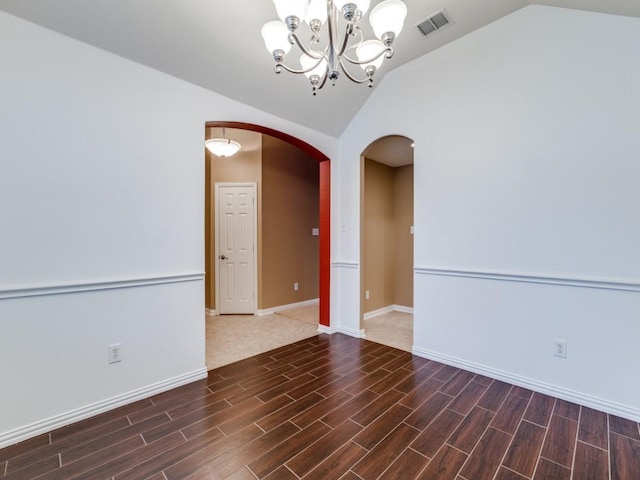 unfurnished room featuring wood finished floors, visible vents, vaulted ceiling, and arched walkways
