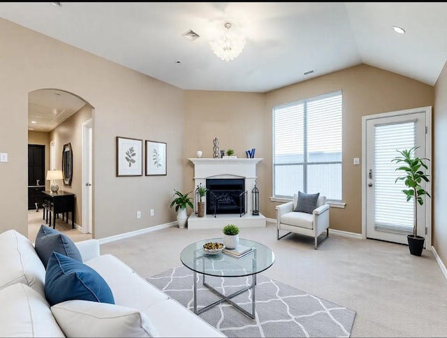 living room featuring an inviting chandelier, a fireplace with raised hearth, plenty of natural light, and light carpet