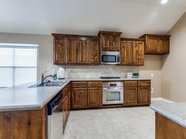 kitchen with decorative backsplash, a sink, appliances with stainless steel finishes, light countertops, and a peninsula