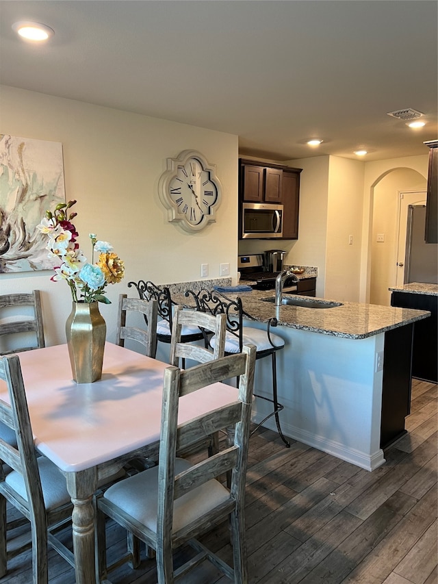 kitchen with sink, stainless steel appliances, dark brown cabinetry, light stone counters, and dark hardwood / wood-style floors