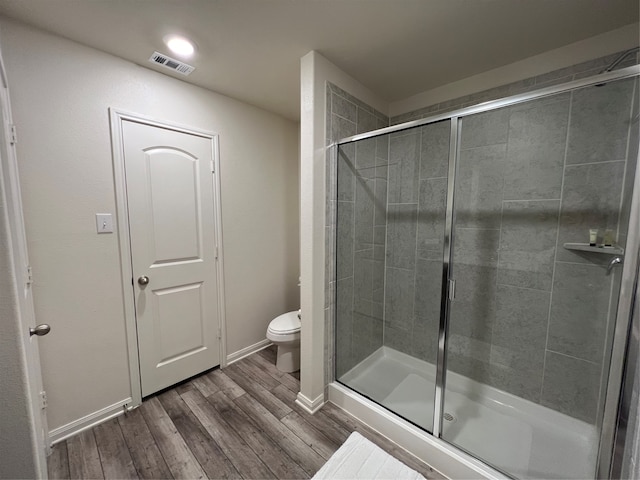 bathroom with hardwood / wood-style floors, a shower with shower door, and toilet