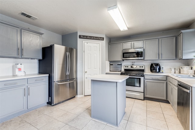 kitchen with gray cabinetry, stainless steel appliances, light tile patterned floors, and a kitchen island