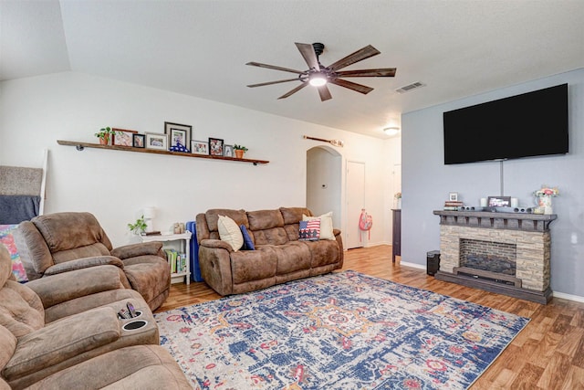 living room featuring a stone fireplace, ceiling fan, hardwood / wood-style floors, and vaulted ceiling