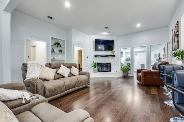 living room with dark hardwood / wood-style flooring, a brick fireplace, and built in features