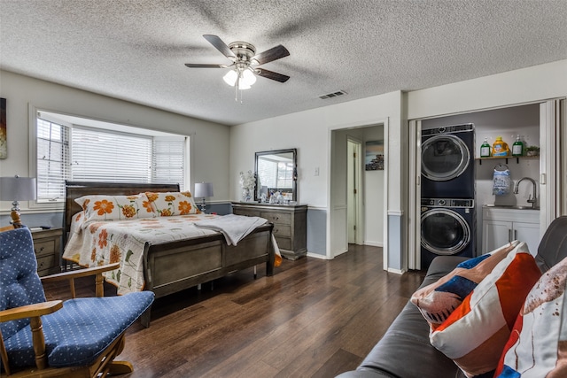 bedroom featuring stacked washer / drying machine, sink, a textured ceiling, dark hardwood / wood-style flooring, and ceiling fan