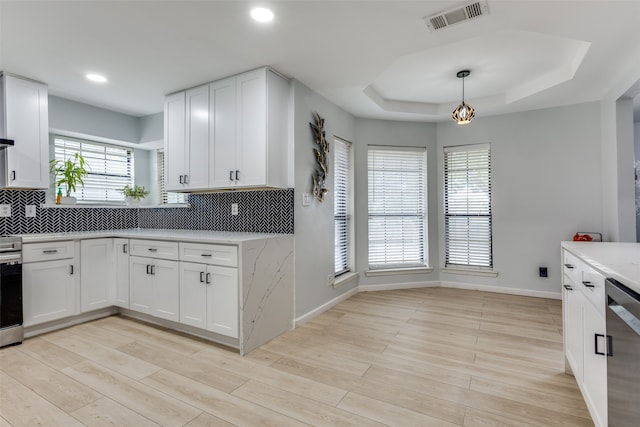 kitchen with white cabinets, hanging light fixtures, stainless steel dishwasher, light hardwood / wood-style floors, and a raised ceiling