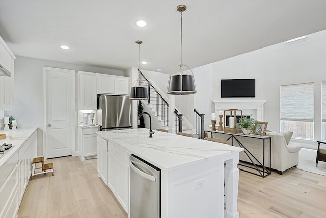 kitchen featuring a center island with sink, light stone counters, hanging light fixtures, white cabinets, and light wood-type flooring