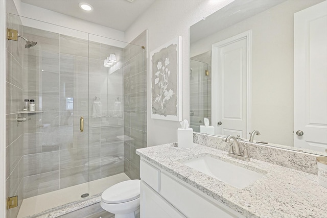 bathroom featuring a shower with door, vanity, and toilet