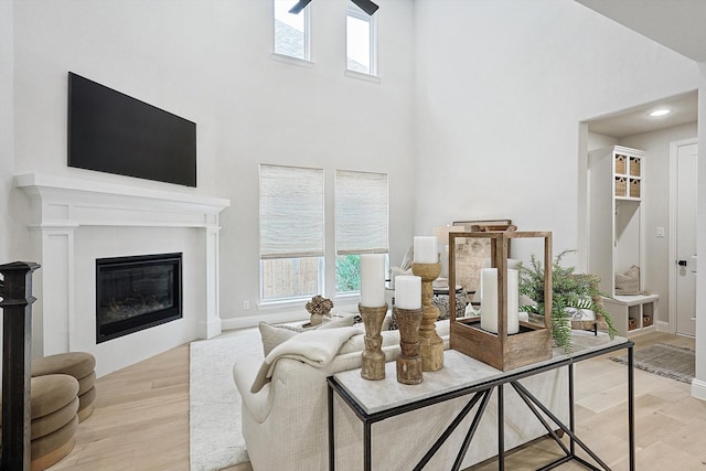 living room with ceiling fan, a towering ceiling, light hardwood / wood-style floors, and a fireplace