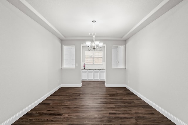 unfurnished dining area with a chandelier, a raised ceiling, dark wood finished floors, and baseboards