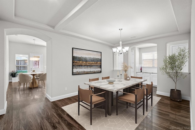 dining space with arched walkways, a raised ceiling, dark wood-type flooring, a chandelier, and baseboards