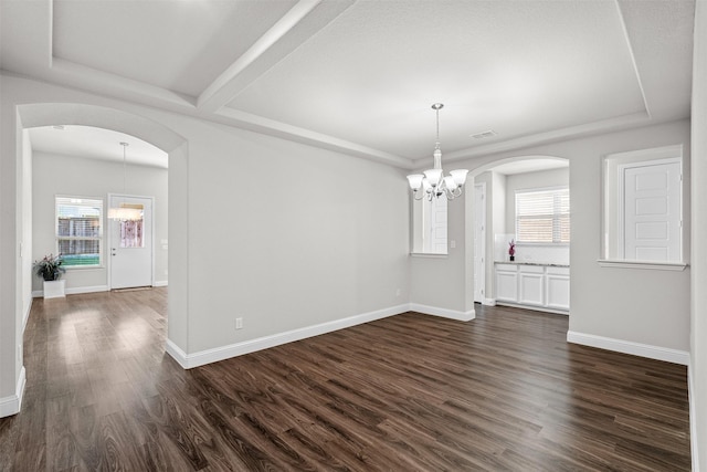 unfurnished dining area with baseboards, arched walkways, dark wood finished floors, a tray ceiling, and a notable chandelier