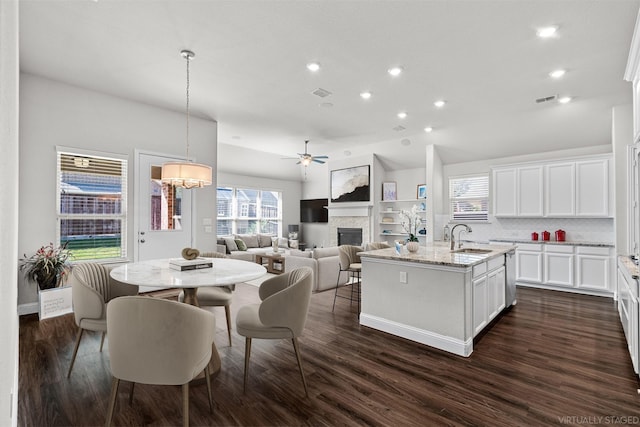 kitchen featuring light stone counters, a fireplace, dark wood-type flooring, a kitchen island with sink, and a sink