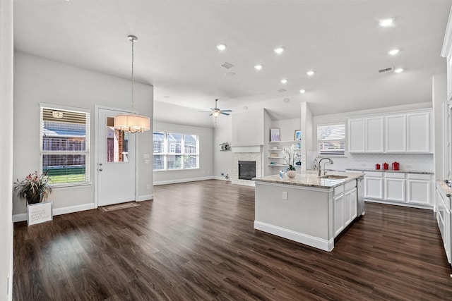 kitchen with open floor plan, light stone countertops, a kitchen island with sink, a fireplace, and a sink