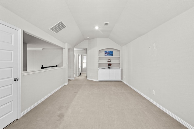 interior space featuring light carpet, visible vents, built in features, baseboards, and vaulted ceiling