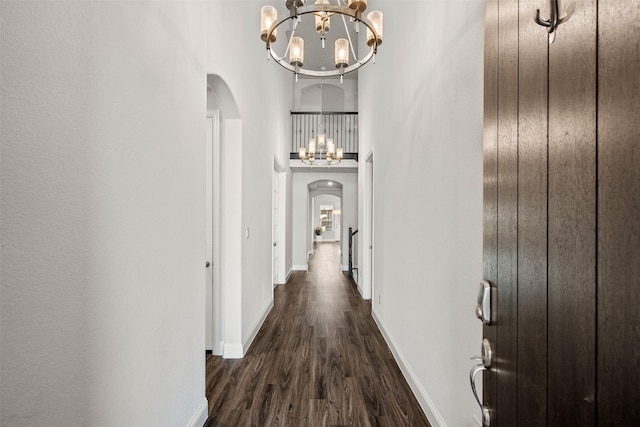 hallway with a towering ceiling, a notable chandelier, and dark hardwood / wood-style floors