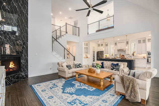 living room with sink, dark hardwood / wood-style flooring, a fireplace, a towering ceiling, and ceiling fan