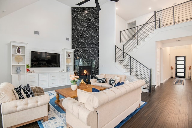 living room featuring dark wood-type flooring, ceiling fan, a towering ceiling, and a high end fireplace