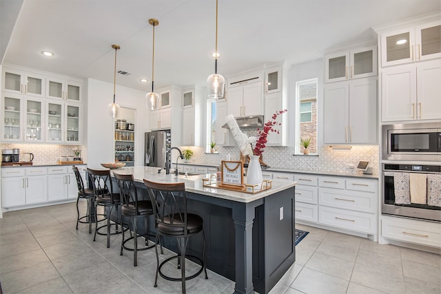 kitchen featuring decorative backsplash, a kitchen island with sink, stainless steel appliances, decorative light fixtures, and white cabinetry