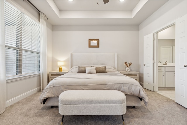 bedroom with ceiling fan, light colored carpet, a tray ceiling, and connected bathroom