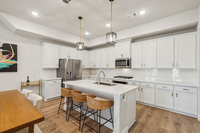 kitchen featuring white cabinetry, stainless steel appliances, hanging light fixtures, a breakfast bar, and sink