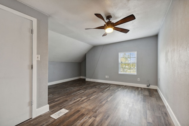 additional living space with a textured ceiling, ceiling fan, dark wood-type flooring, and vaulted ceiling