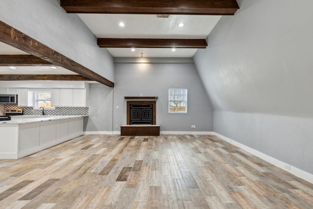 unfurnished living room featuring beam ceiling, sink, and light hardwood / wood-style flooring