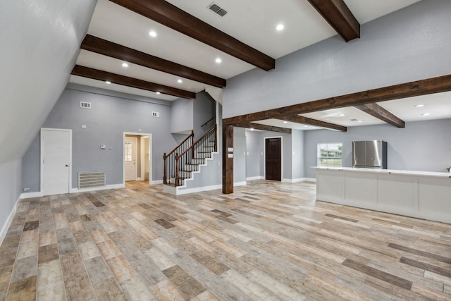 unfurnished living room with beamed ceiling, light hardwood / wood-style floors, and a high ceiling