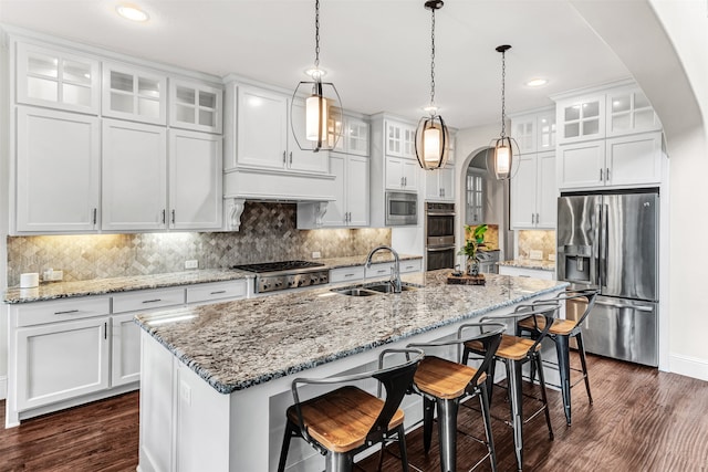 kitchen with a kitchen island with sink, hanging light fixtures, stainless steel appliances, sink, and white cabinets