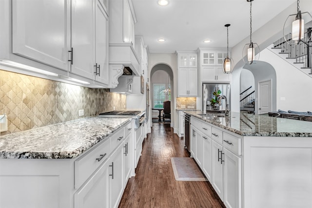 kitchen with a center island with sink, white cabinetry, stainless steel appliances, pendant lighting, and dark hardwood / wood-style floors