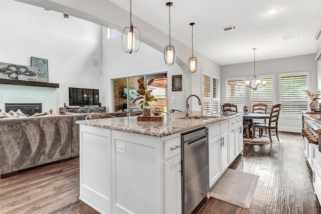 kitchen with light stone countertops, sink, stainless steel dishwasher, white cabinets, and a kitchen island with sink