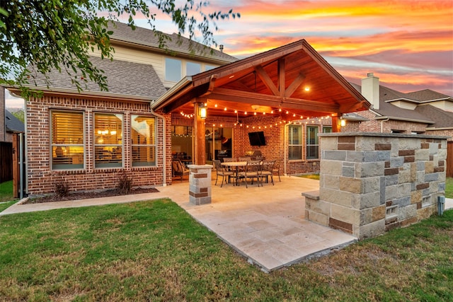 back house at dusk with a patio area and a lawn