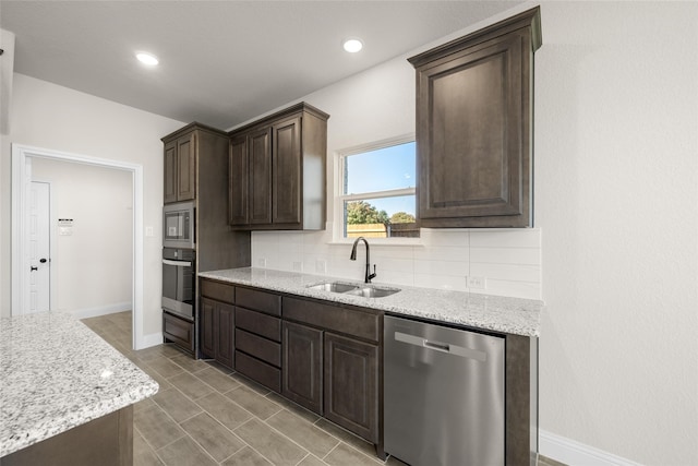 kitchen featuring appliances with stainless steel finishes, sink, decorative backsplash, dark brown cabinetry, and light stone counters