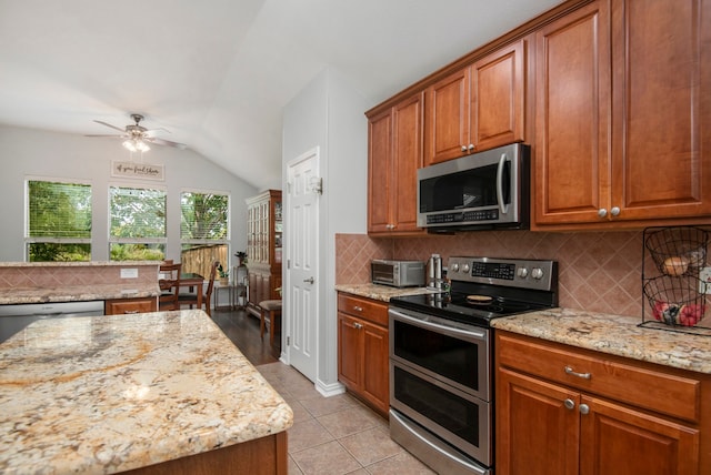 kitchen featuring stainless steel appliances, light stone countertops, vaulted ceiling, and tasteful backsplash