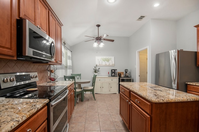 kitchen with stainless steel appliances, light stone countertops, light tile patterned floors, a center island, and vaulted ceiling