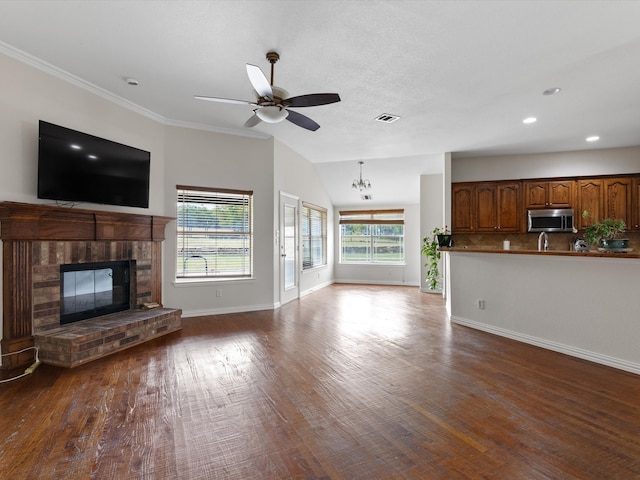 unfurnished living room featuring wood-type flooring, ceiling fan with notable chandelier, a fireplace, lofted ceiling, and ornamental molding