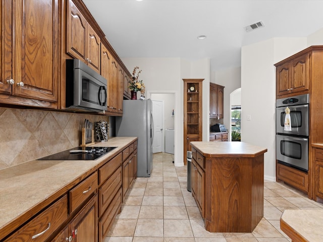 kitchen with a kitchen island, light tile patterned flooring, stainless steel appliances, and tasteful backsplash