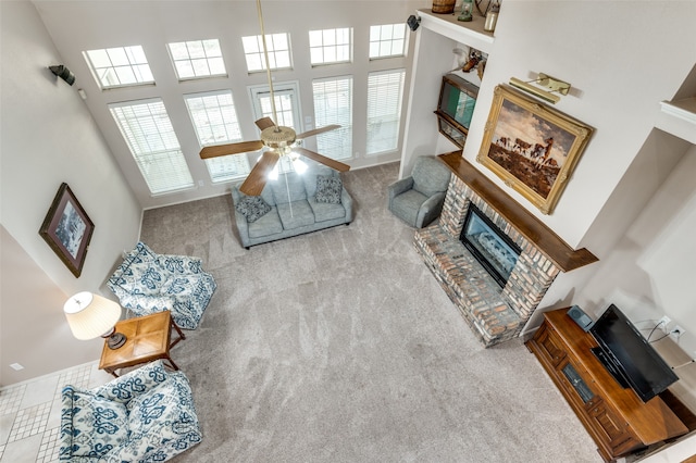 carpeted living room with a towering ceiling, a fireplace, and ceiling fan