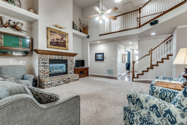 living room featuring carpet flooring, a towering ceiling, a brick fireplace, and ceiling fan