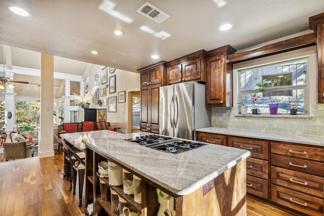 kitchen with a breakfast bar area, a kitchen island, stainless steel appliances, light stone countertops, and decorative backsplash