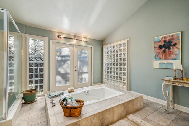 bathroom with french doors, vaulted ceiling, and tiled tub