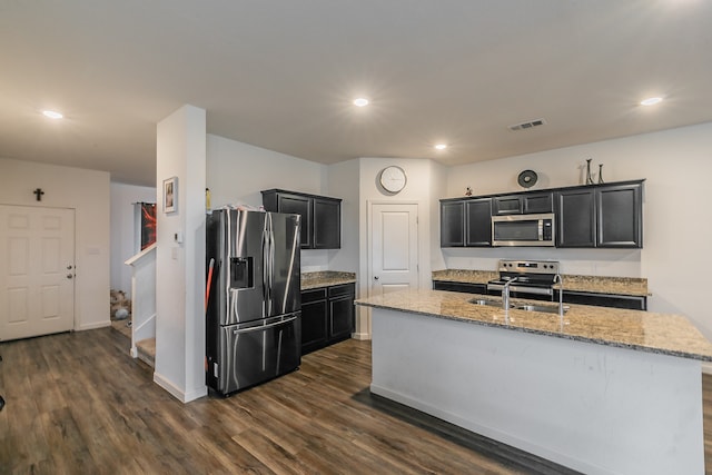 kitchen with a center island with sink, appliances with stainless steel finishes, dark hardwood / wood-style floors, sink, and light stone counters