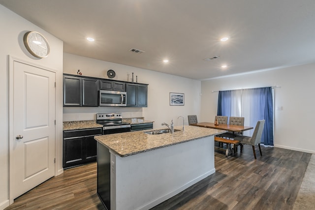 kitchen with light stone counters, dark hardwood / wood-style flooring, an island with sink, sink, and stainless steel appliances