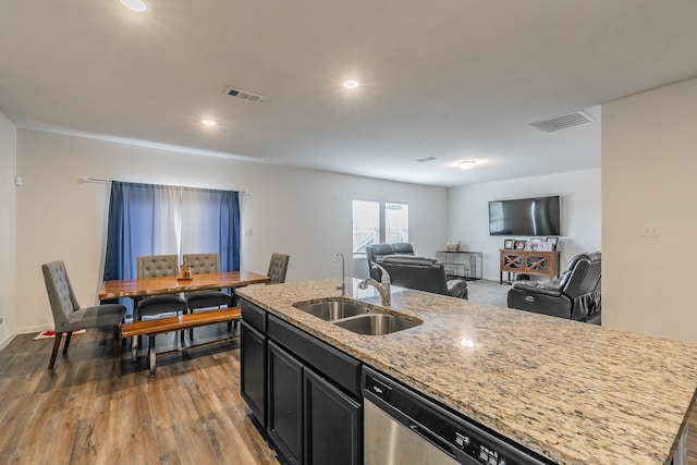 kitchen with dishwasher, a kitchen island with sink, dark hardwood / wood-style floors, sink, and light stone counters