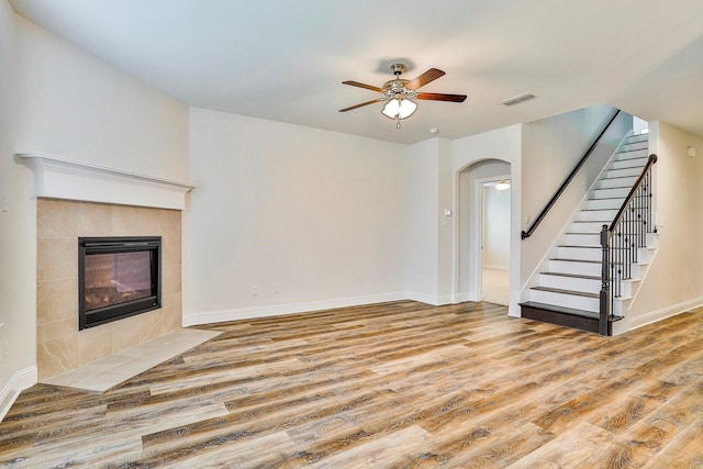 unfurnished living room with wood-type flooring, a tile fireplace, and ceiling fan