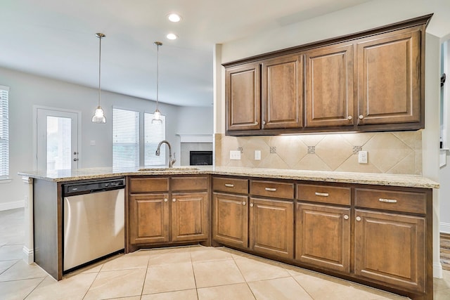 kitchen with decorative backsplash, dishwasher, hanging light fixtures, sink, and light stone countertops