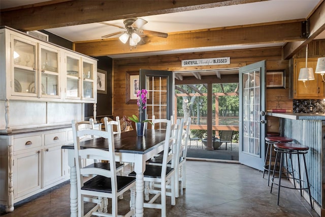 dining space featuring beam ceiling, wood walls, and ceiling fan